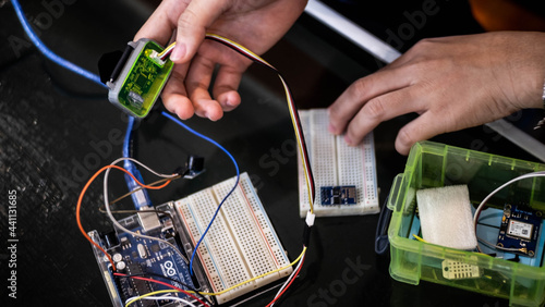 Detailed close-up of an Arduino Uno circuit in progress. Jumper wires connect to a breadboard, while one hand holds a small component and the other supports the electronic assembly process.