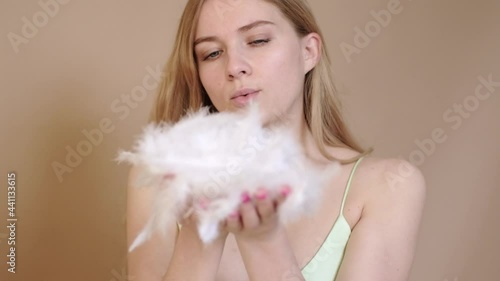 slow motion beauty portrait beautiful blonde woman playfully blowing feathers in beige background