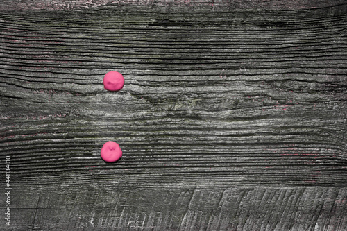 Two pink dots, painted with squeezed paint from a tube on an old wooden board, a colon punctuation mark or mathematical division sign. photo