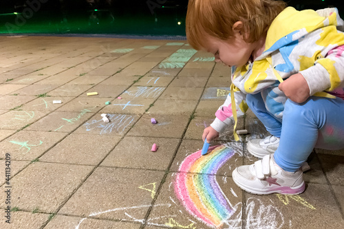 A child draws a rainbow with multi-colored crayons on a summer evening outside the premises. 