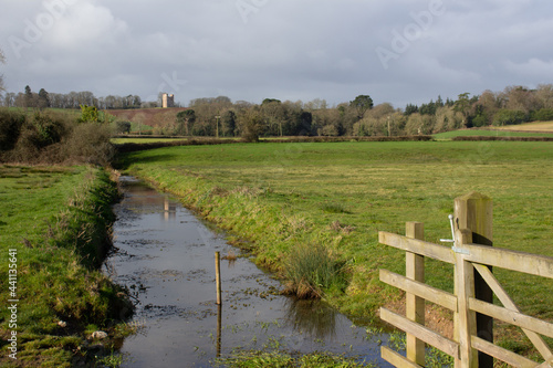 drainage channel and agte in typical English farmland with Folly in the distance and a blue sky and white clouds