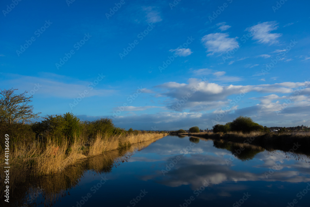 Exeter Ship Canal at Topsham with a few clouds reflected in the still water and a clear blue sky
