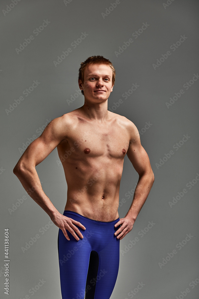 Young athlete swimmer, in shorts on a gray background, portrait of an athlete swimmer in the studio