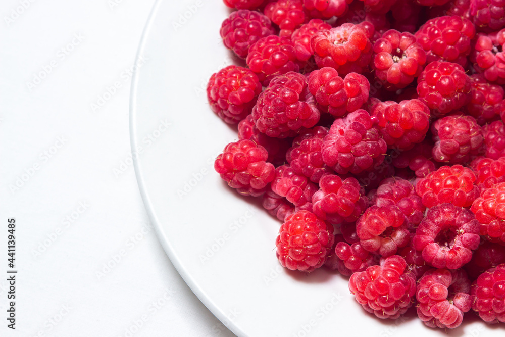 Raspberries in a plate on a white background. Red ripe raspberries close-up. Delicious berry