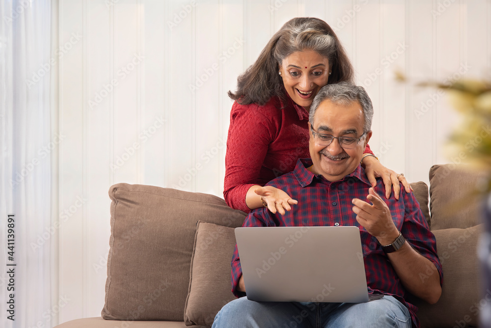 A HUSBAND AND WIFE LOOKING AT LAPTOP IN SURPRISE A HUSBAND AND WIFE LOOKING AT LAPTOP IN SURPRISE