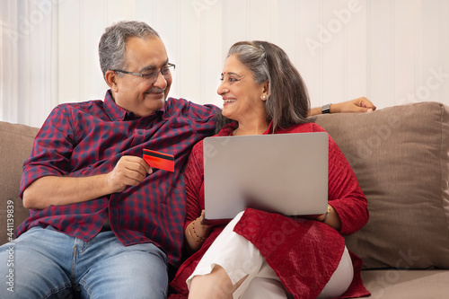 AN OLD COUPLE HAPPILY LOOKING AT EACH OTHER WHILE DOING ONLINE TRANSACTION photo