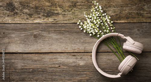 beige wireless headphones on a wooden table, next to a bouquet of white lilies of the valley