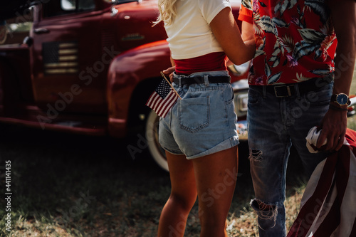 A couple with their vintage truck - 4th of july American Independence Day, a couple wrapped in a usa flag, sit together in preparation for the fireworks - happy young couple holding American flag 