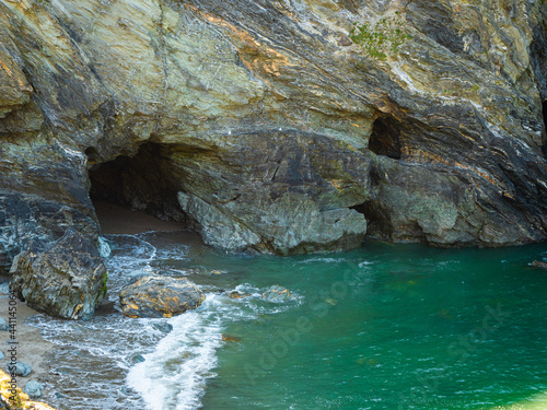 Coastal waves lap around Merlin’s Cave in the bay beside Tintagel Island off the rugged north coast of Cornwall, UK, a centre of British legends about King Arthur and his mentoring wizard.