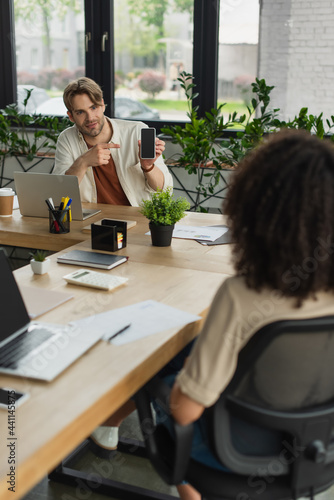 young man pointing with finger to smartphone screen near african american colleague in office © LIGHTFIELD STUDIOS