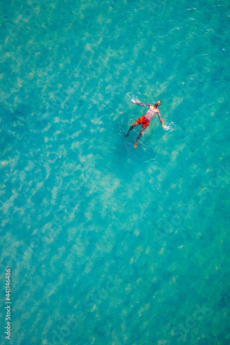 Drone view of a man floating in tropical sea water. Aerial view of young man floating on sea water enjoying sunbathing and vacations in tropical destination. People travel tourism holidays concept.