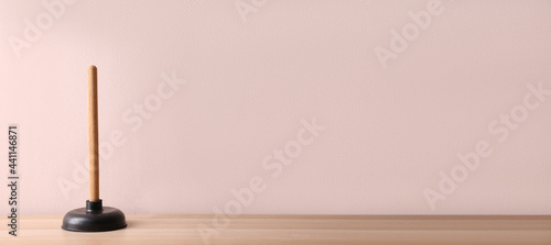 Plunger on wooden table against pink background. Space for text photo