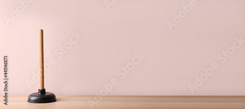 Plunger on wooden table against pink background. Space for text