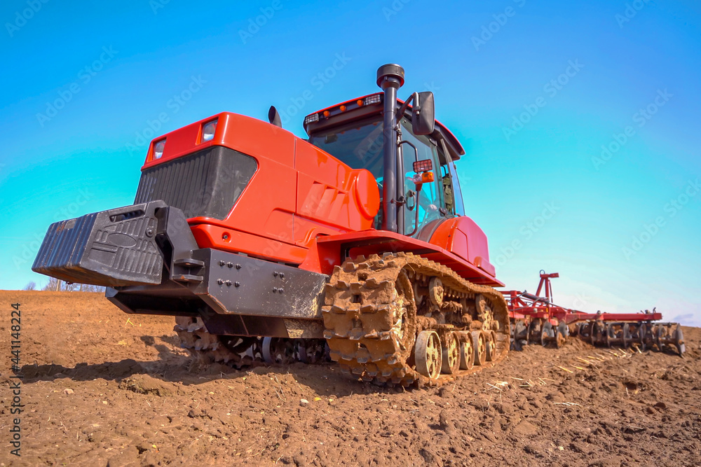 A heavy tracked tractor plows and buries a field in early spring against the blue sky.