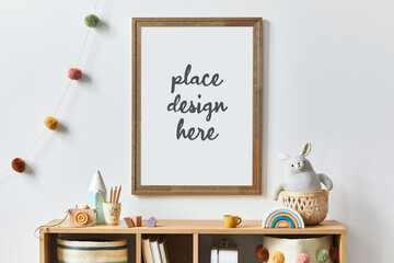Stylish scandinavian newborn baby room with brown wooden mock up poster frame, toys, plush animal and child accessories. Cozy decoration and hanging cotton flags on the white wall. Template.
