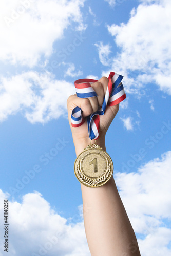 Hand of woman holding gold medal against sky.award and victory concept.copy space