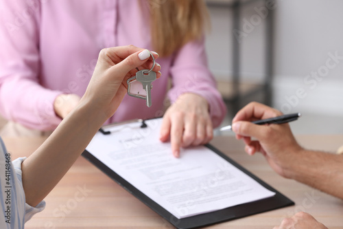Woman holding new house key in real estate agent's office, closeup