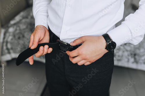 A man  a businessman is going to work in the morning  buttoning a black leather belt with his hands. Photography  concept.