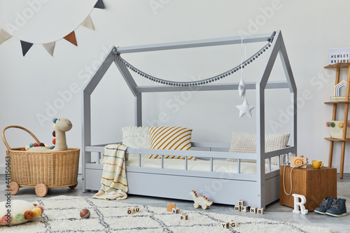 Stylish scandinavian child's room with creative wooden bed, rattan basket, wooden shelf, plush and wooden toys and hanging textile decorations. Grey walls, carpetn on the floor. Template. photo