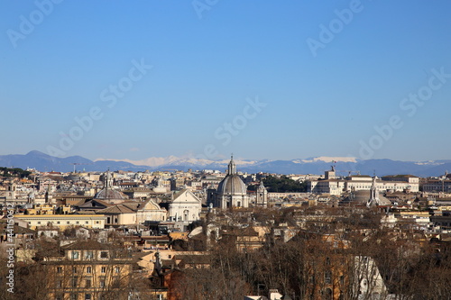 Top view of the rooftops and churches of Rome, Italy, on a cold winter day with snow capped white mountains