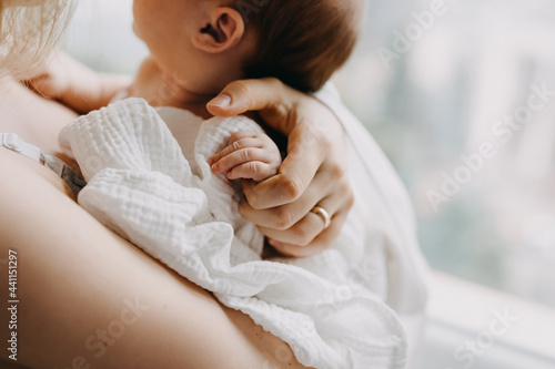 Closeup of mother holding newborn baby hand, standing by the window.