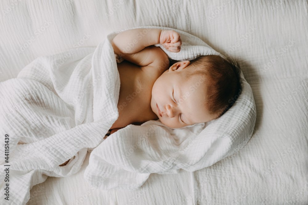 Newborn baby sleeping in a baby nest, covered with white muslin blanket. - obrazy, fototapety, plakaty 