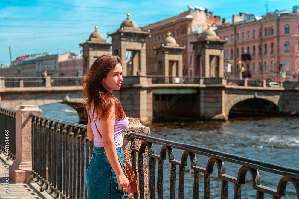 A beautiful young woman walks in the center of St. Petersburg on the embankment with a beautiful bridge