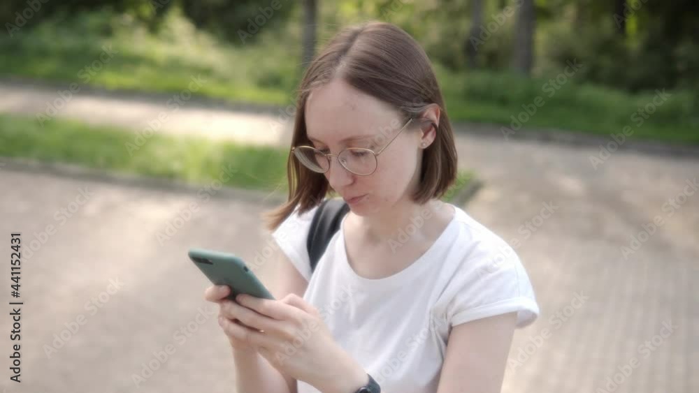 Attractive student girl in glasses with a short haircut chatting using a smartphone. Attractive student girl in glasses with a short haircut chatting using a smartphone.
