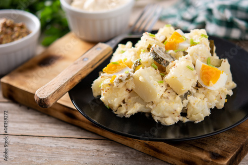 Potato salad with gherkins, egg and mustard on wooden table