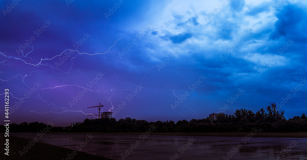 Fototapeta premium Landscape photo of big thunderclouds with many thunders raining down - nice purple and blue sky colors - old german runway in the foreground