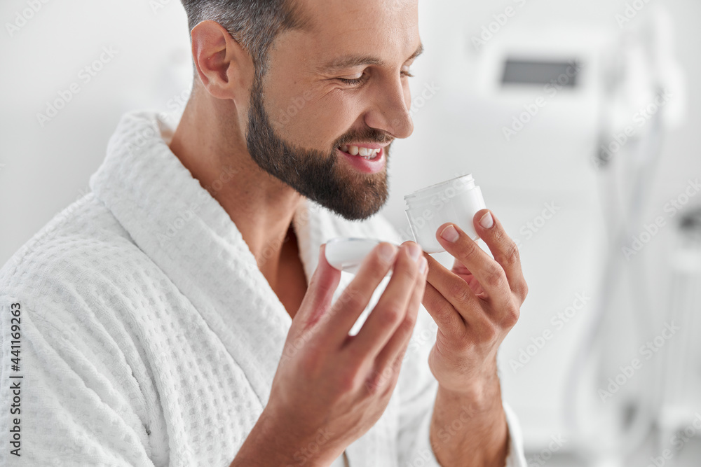 Positive man smells cream in open jar before procedure in cosmetologycal clinic Positive man smells cream in open jar before procedure in cosmetologycal clinic
