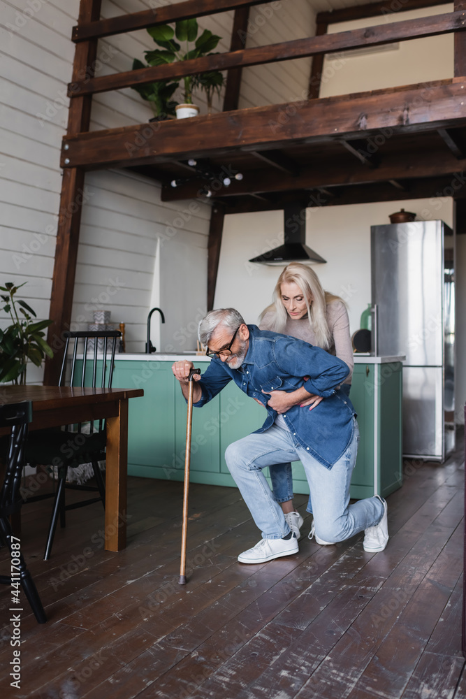 Senior woman helping sick husband with crutch at home