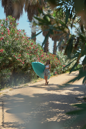 Young woman smiling with her paddle surf board on a beach path