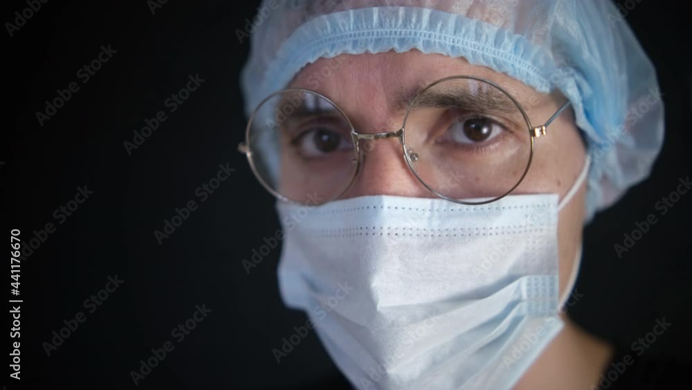 A doctor wearing a mask and anti-coronavirus glasses looks into the camera. Close-up. Black background A doctor wearing a mask and anti-coronavirus glasses looks into the camera. Close-up. Black background