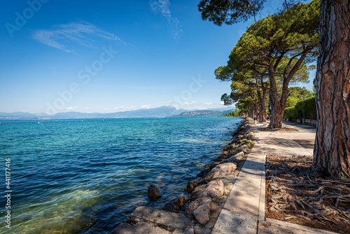 Fototapeta Naklejka Na Ścianę i Meble -  Coast of Lake Garda (Lago di Garda) in front of the small Lazise village, Tourist resort in Verona province, Veneto, Italy, southern Europe. In the background the coastline of Lombardy.