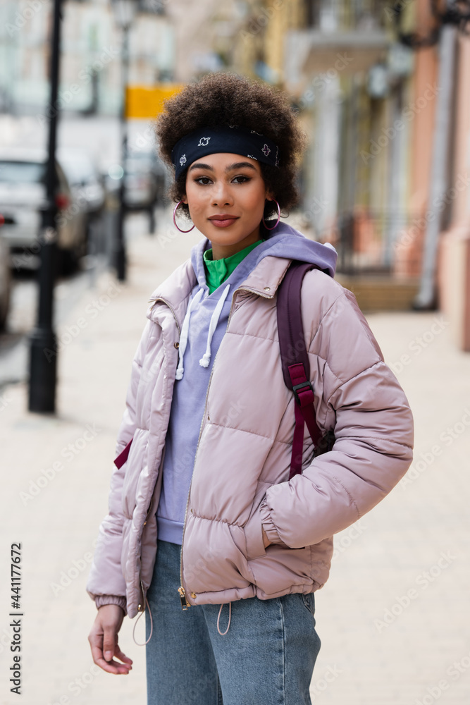 Obraz premium African american woman in jacket looking at camera on urban street