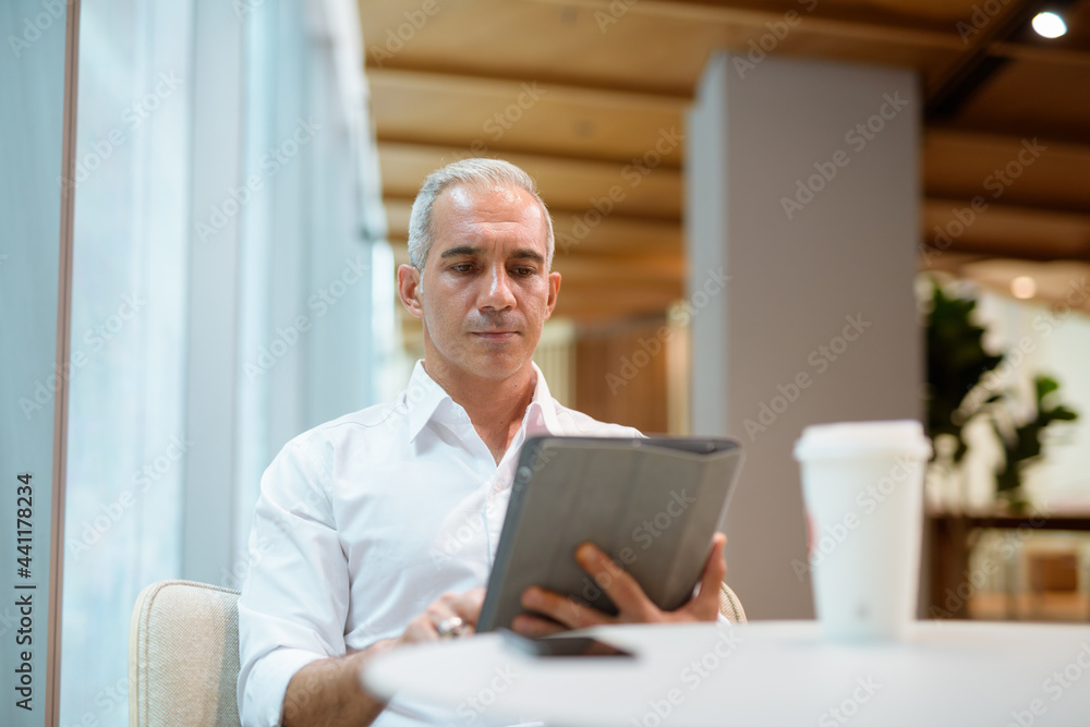 Portrait of handsome businessman sitting at coffee shop and using digital tablet Portrait of handsome businessman sitting at coffee shop and using digital tablet
