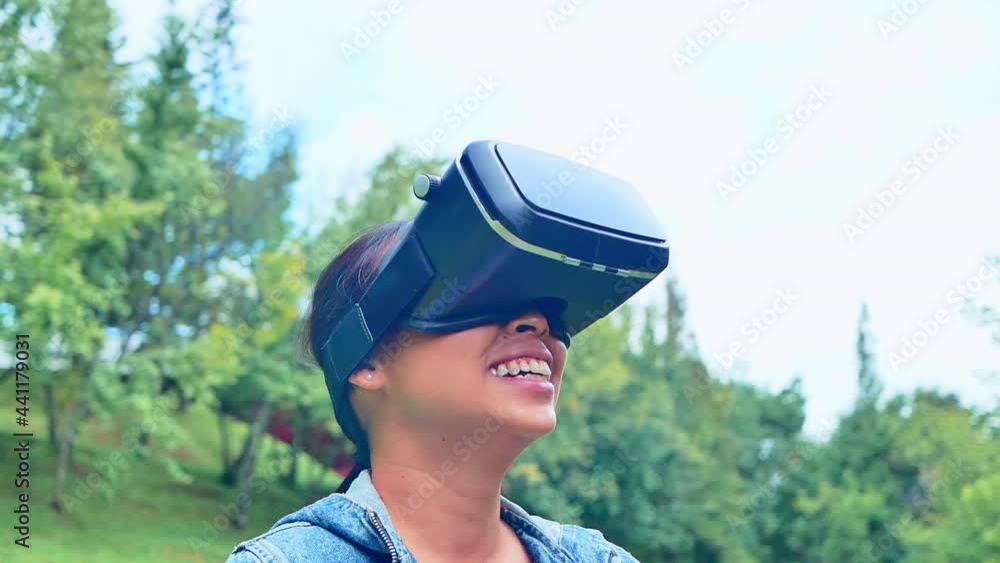 Happy woman wearing VR-headset glasses of virtual reality in forest and enjoying the nature on a sunny summer day in spring garden. Modern technology concept. Happy woman wearing VR-headset glasses of virtual reality in forest and enjoying the nature on a sunny summer day in spring garden. Modern technology concept.
