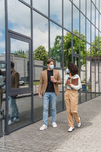 young interracial colleagues in medical masks walking with coffee paper cups near modern building © LIGHTFIELD STUDIOS