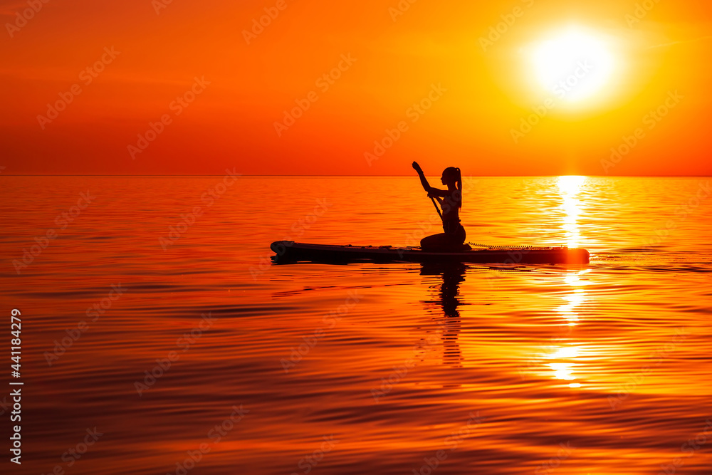 Girl on stand up paddle board at quiet sea with bright sunset or sunrise. Woman paddle on sup board in sea.