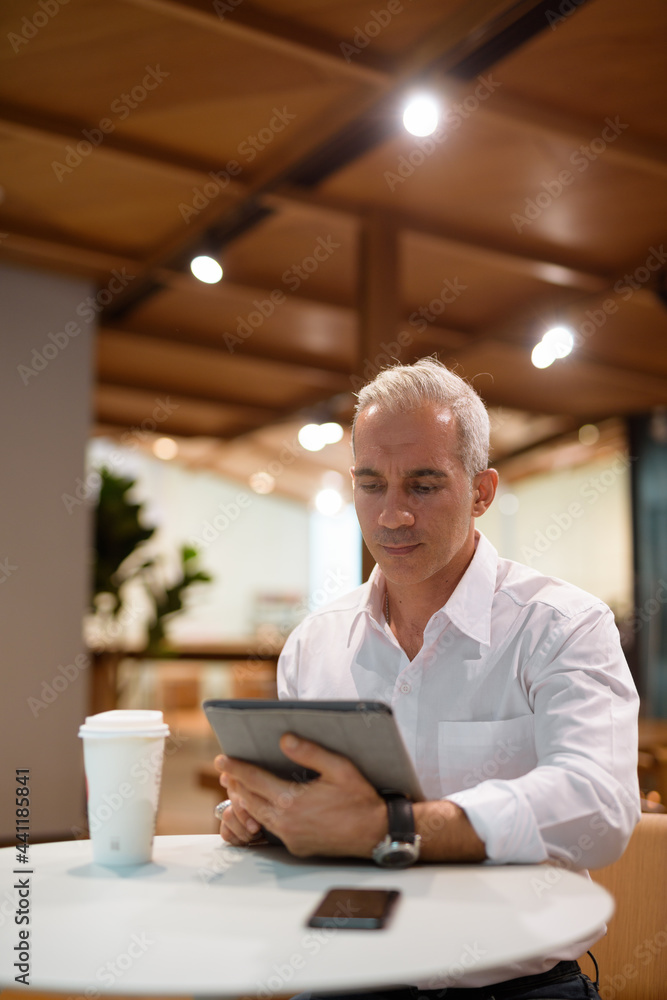 Portrait of handsome businessman sitting at coffee shop and using digital tablet Portrait of handsome businessman sitting at coffee shop and using digital tablet
