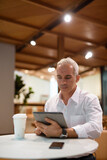 Portrait of handsome businessman sitting at coffee shop and using digital tablet