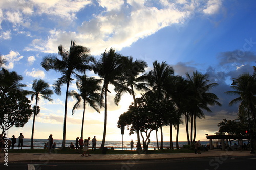 名b\んごくリゾート、ハワイ・ホノルル、ワイキキビーチ。ヤシの木の浜辺に沈む夕日と、人々のシルエット。