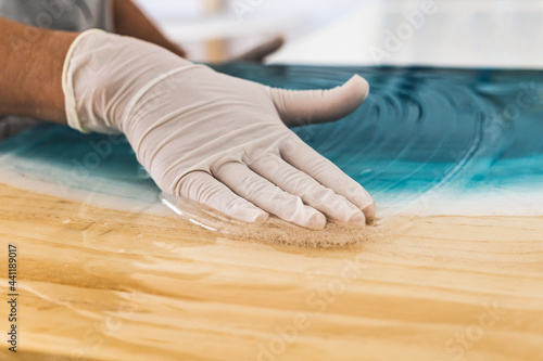 Female artist in protective gloves spreading white epoxy resin onto turquoise color photo