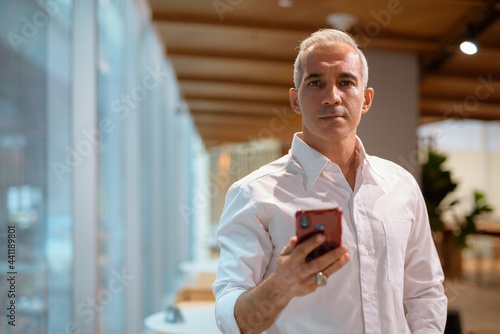 Portrait of handsome businessman at coffee shop using mobile phone