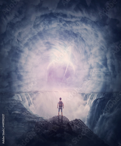 Fotografiet Person stands on the edge of a cliff above a waterfall looking at a huge whirlwind in the clouds that creates a portal to another planet