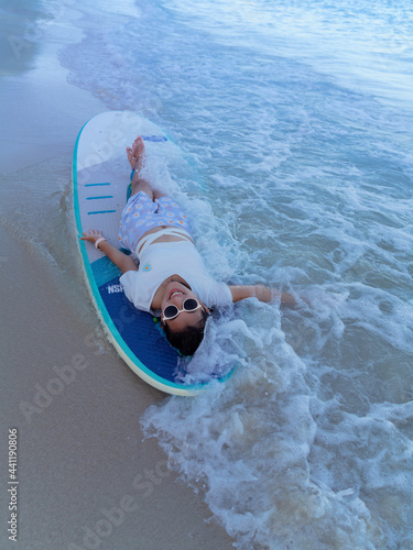 Photography Asian woman with sunglasses laying down on paddleboarding on sand beach with sea