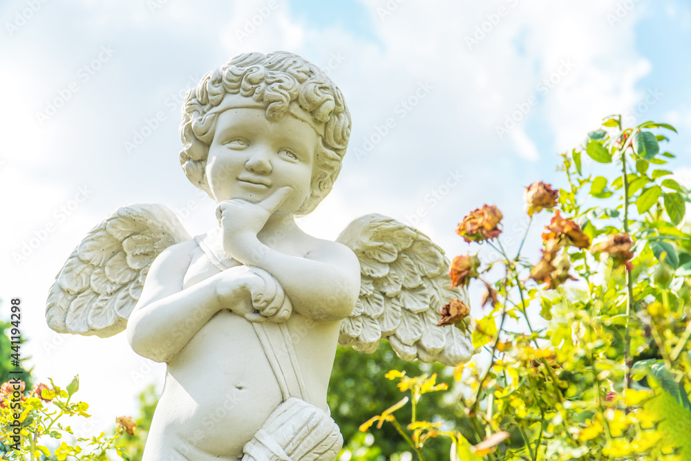 the cute cupid statue in the flower garden the cute cupid statue in the flower garden