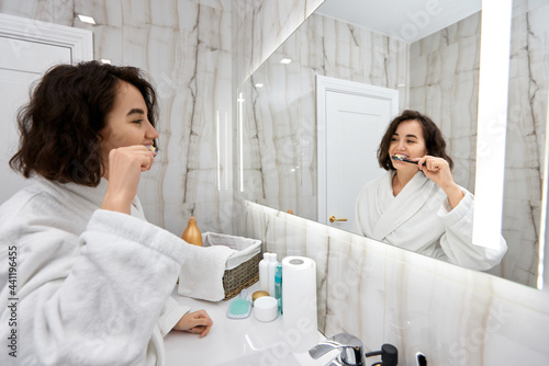 woman in white bathrobes brushing teeth in front of mirror