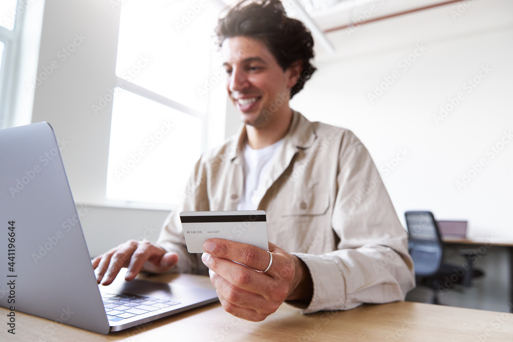 Young man with laptop at desk making business transaction with credit card in open plan office space Young man with laptop at desk making business transaction with credit card in open plan office space